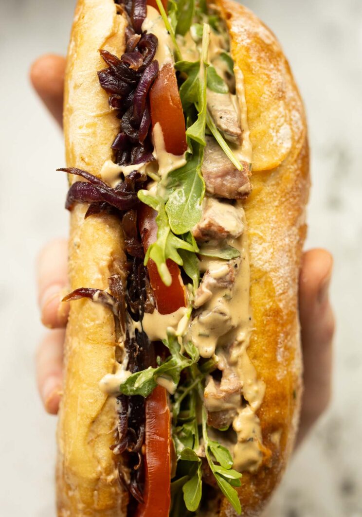 close up overhead shot of hand holding steak sandwich showing filling