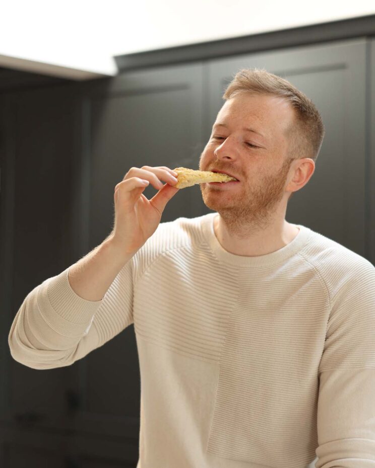 Chris Collins, food blogger at Don't Go Bacon My Heart in white jumper eating a slice of garlic flatbread