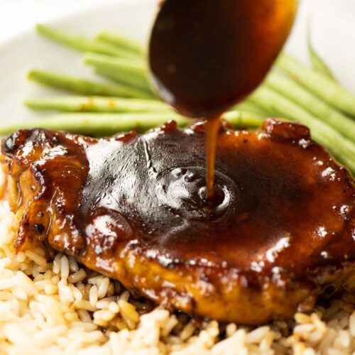 spoon drizzling brown sugar glaze over pork chop on white plate with rice and green beans