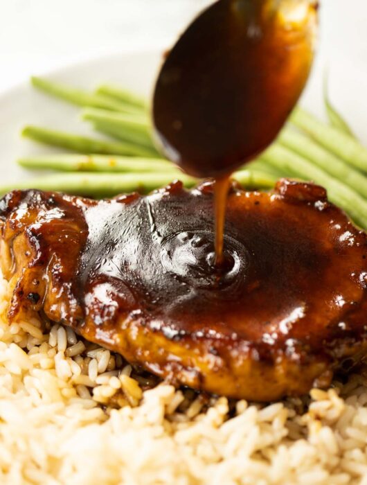 spoon drizzling brown sugar glaze over pork chop on white plate with rice and green beans
