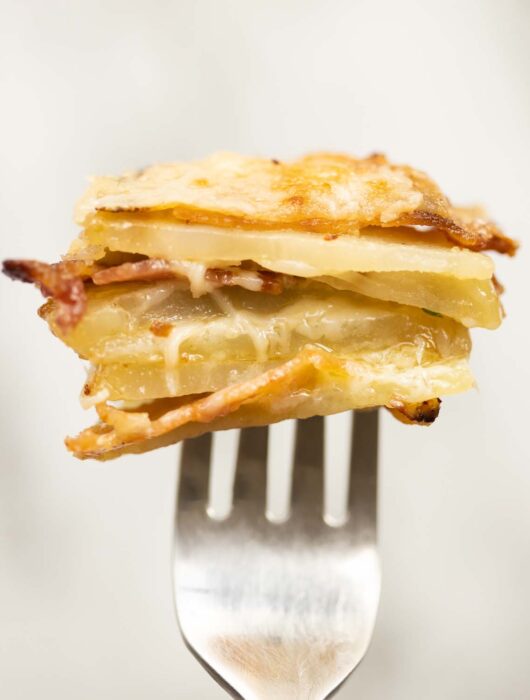 close up shot of half a cheese and bacon potato stacks on silver fork