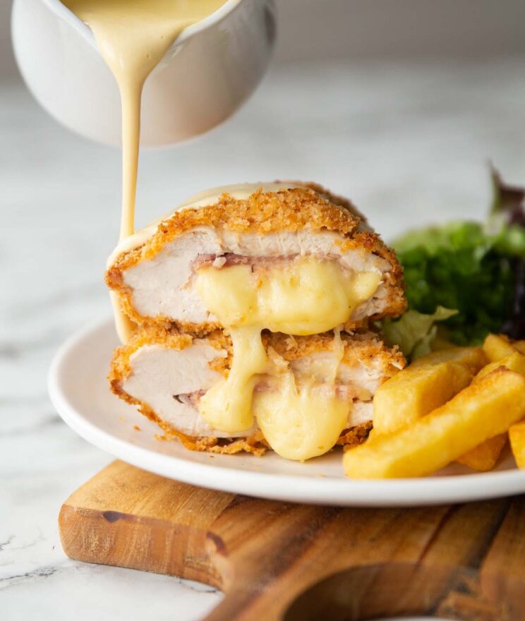 2 chicken cordon bleu halves stacked on each other with small jug pouring sauce over them