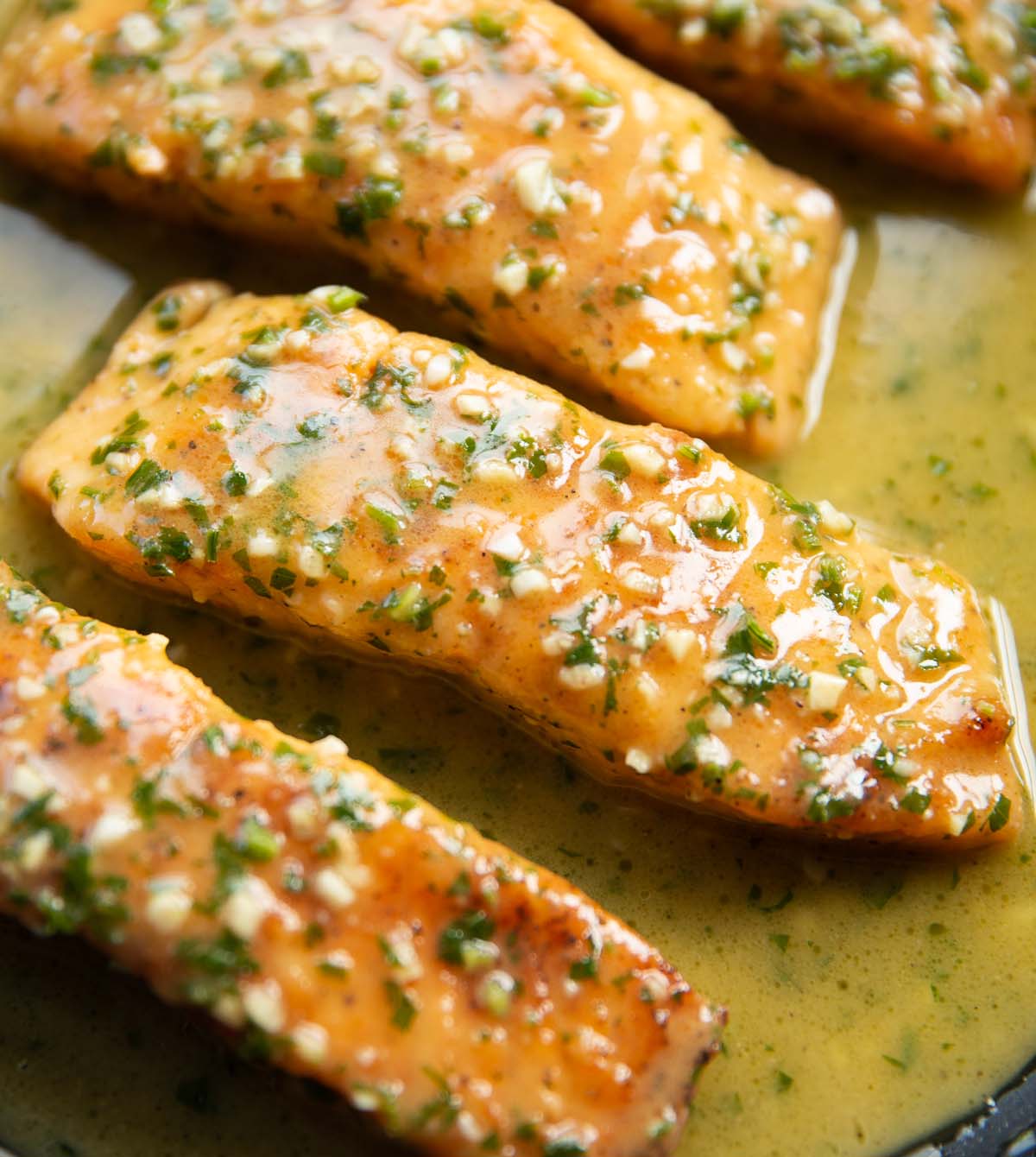 close up shot of garlic butter salmon fillets in frying pan