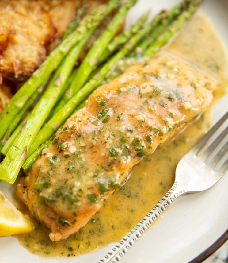 close up shot of garlic butter salmon on white plate with parmesan smashed potatoes and asparagus
