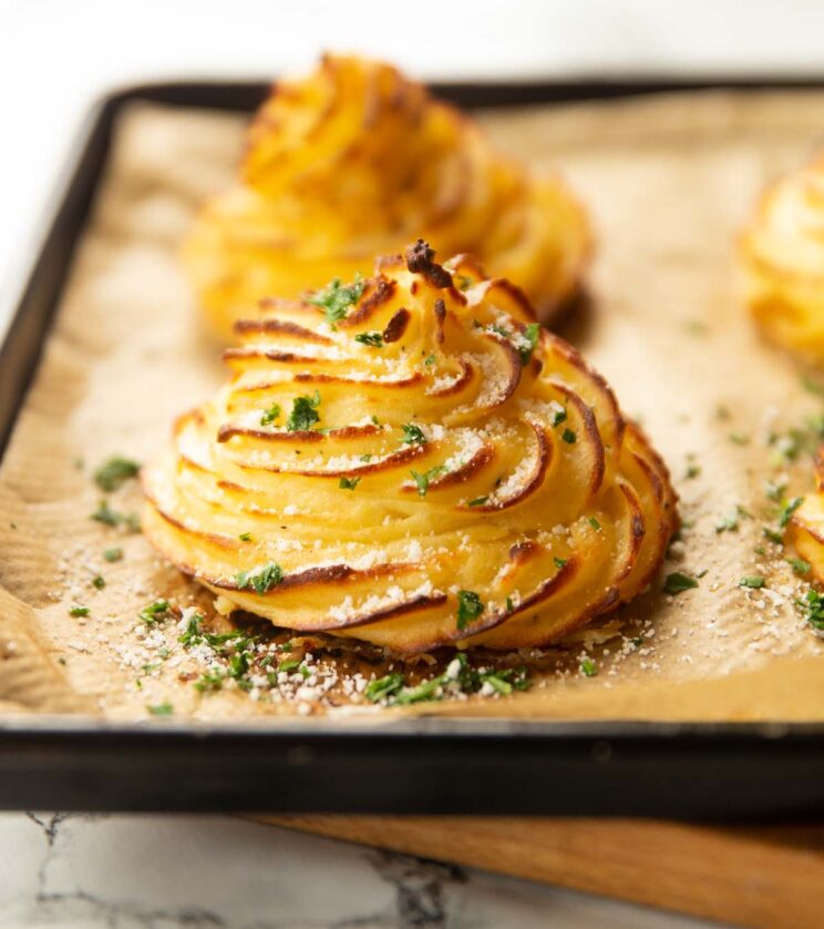 close up shot of garlic parmesan duchess potatoes on baking tray with parmesan and parsley