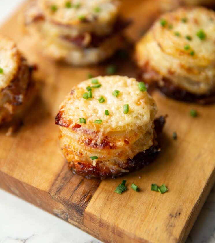 close up shot of gratin potato stacks on chopping board garnished with chives