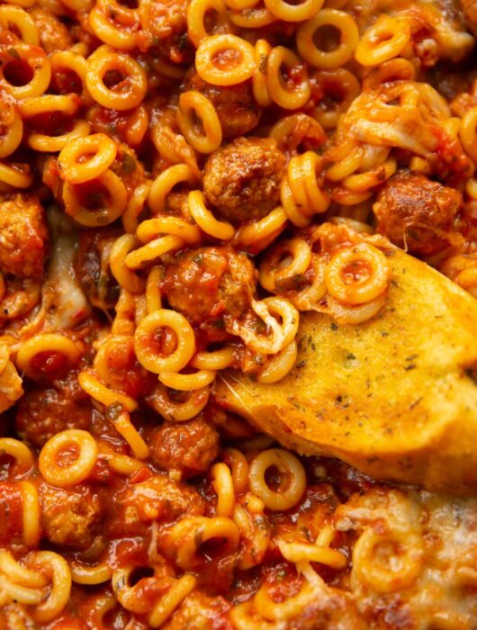 close up overhead shot of garlic bread dunking into pan of spaghetti hoops
