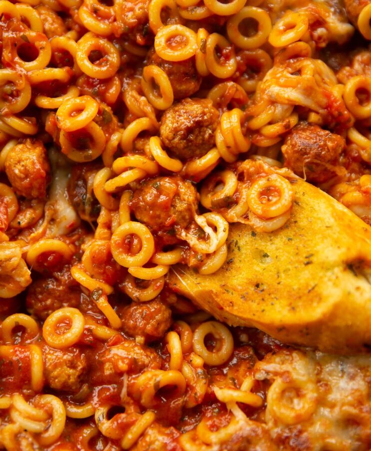 close up overhead shot of garlic bread dunking into pan of spaghetti hoops