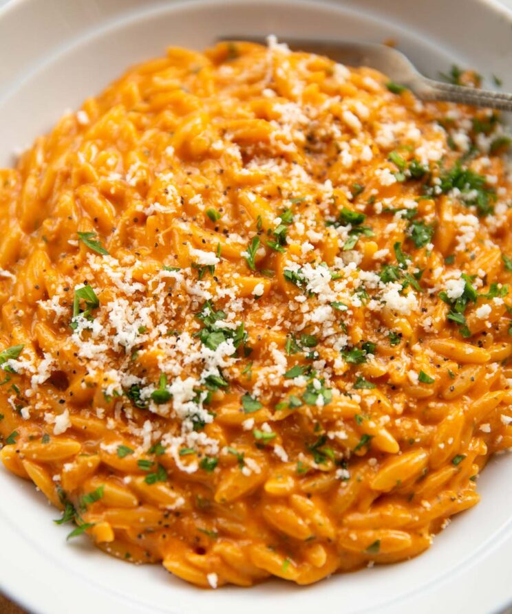close up shot of orzo with 'nduja in large white bowl with parsley and parmesan