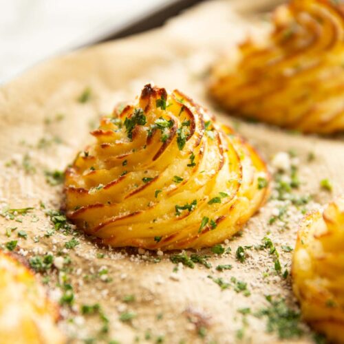 close up shot of parmesan garlic duchess potato on baking sheet garnished with parsley and parmesan