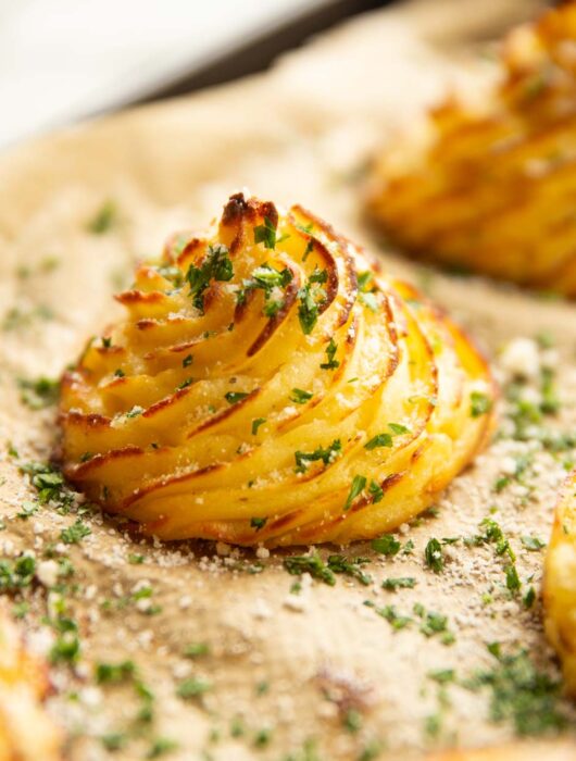 close up shot of parmesan garlic duchess potato on baking sheet garnished with parsley and parmesan