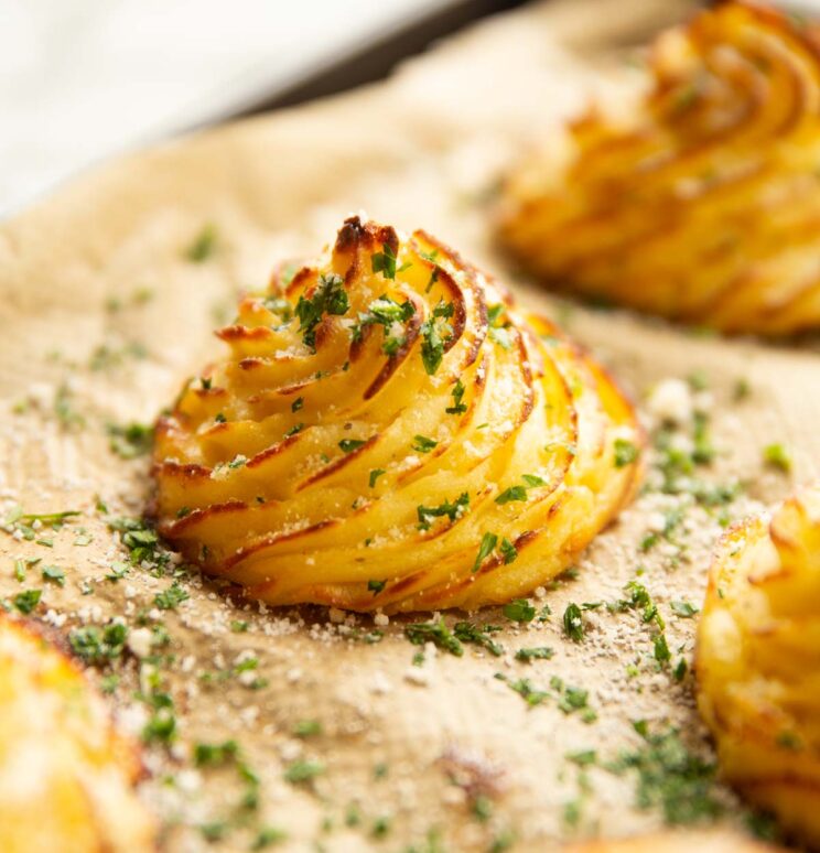 close up shot of parmesan garlic duchess potato on baking sheet garnished with parsley and parmesan