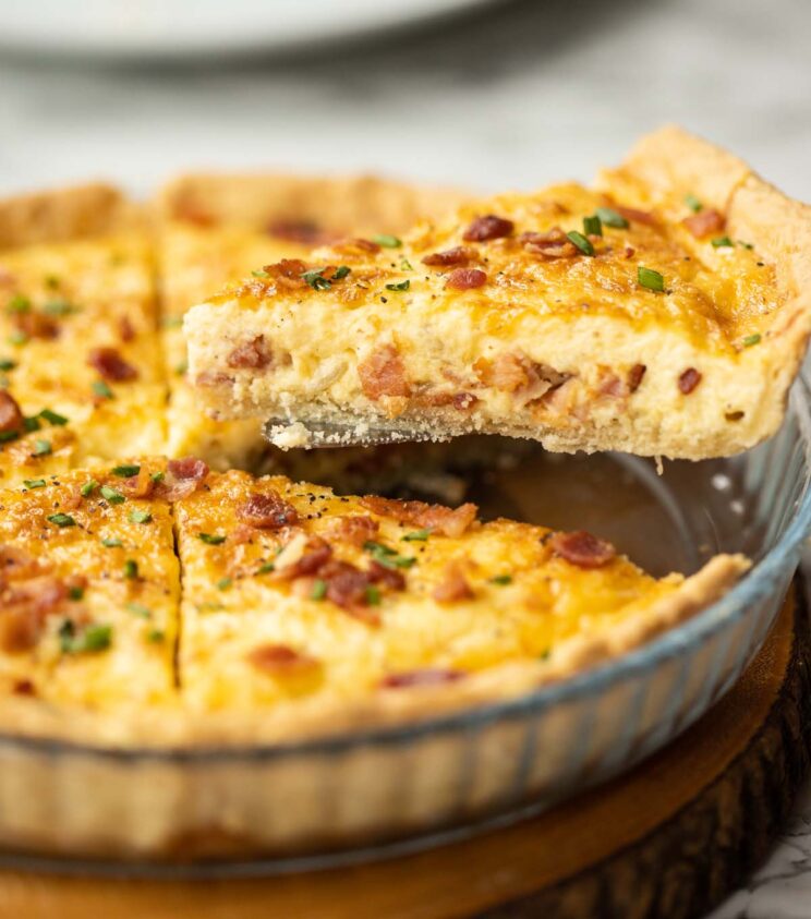 side shot lifting slice of quiche lorraine out of pie dish