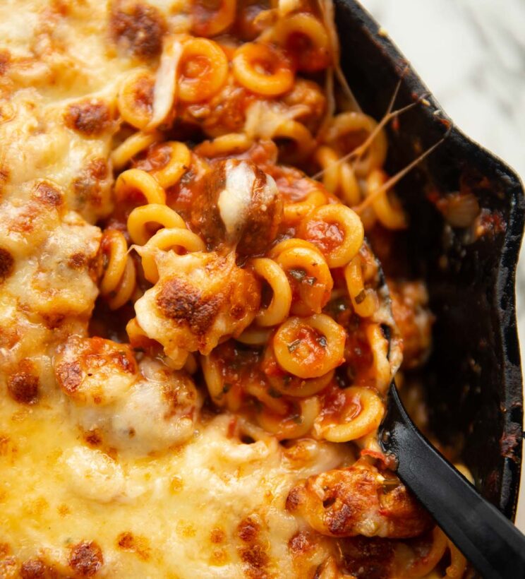 close up shot of serving spoon digging into pan of spaghetti hoops and sausages