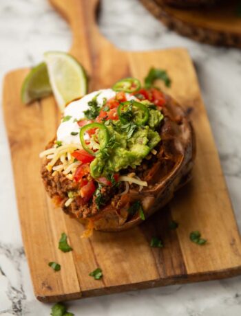 taco stuffed sweet potato on wooden chopping board with limes in background