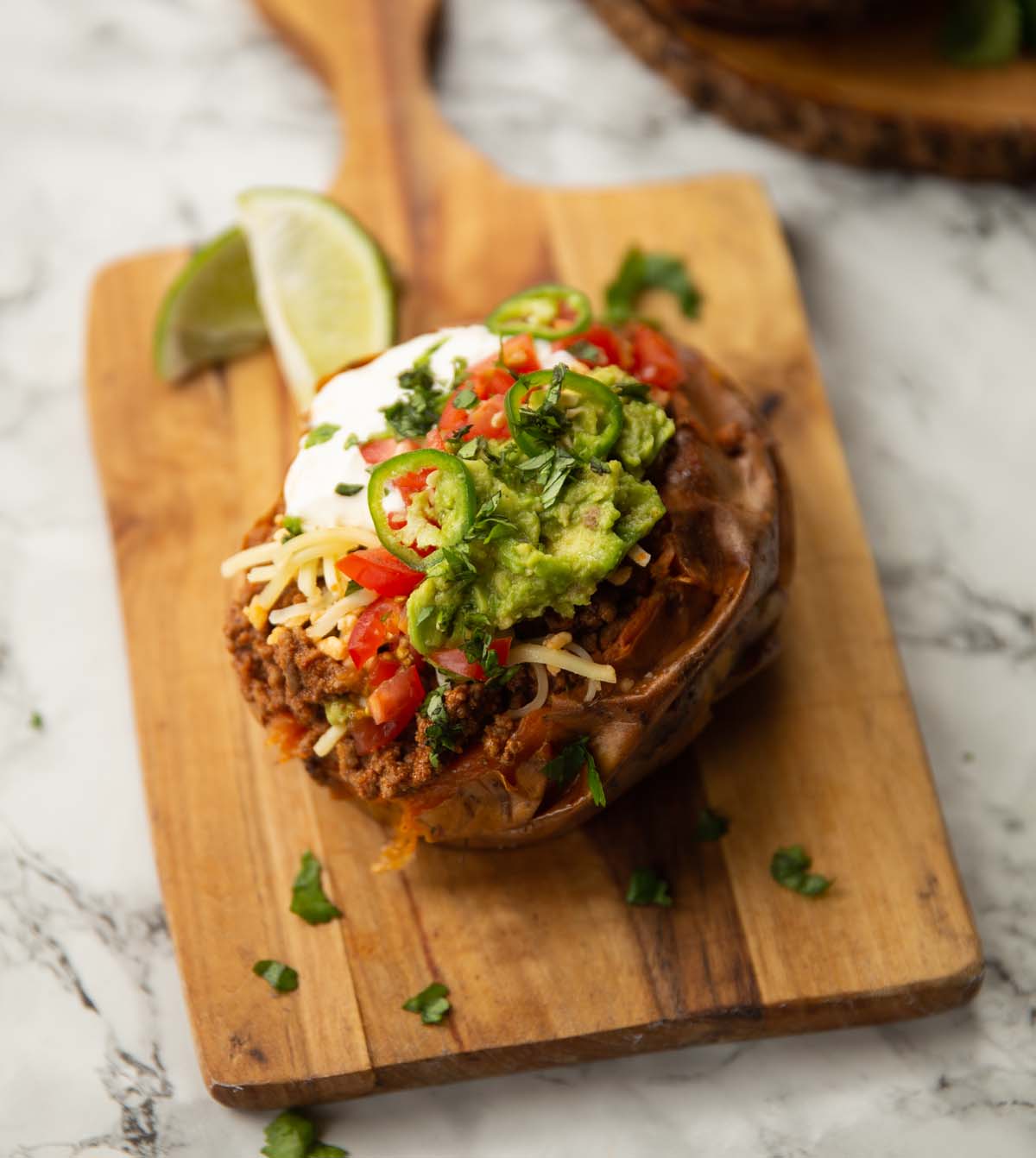 taco stuffed sweet potato on wooden chopping board with limes in background