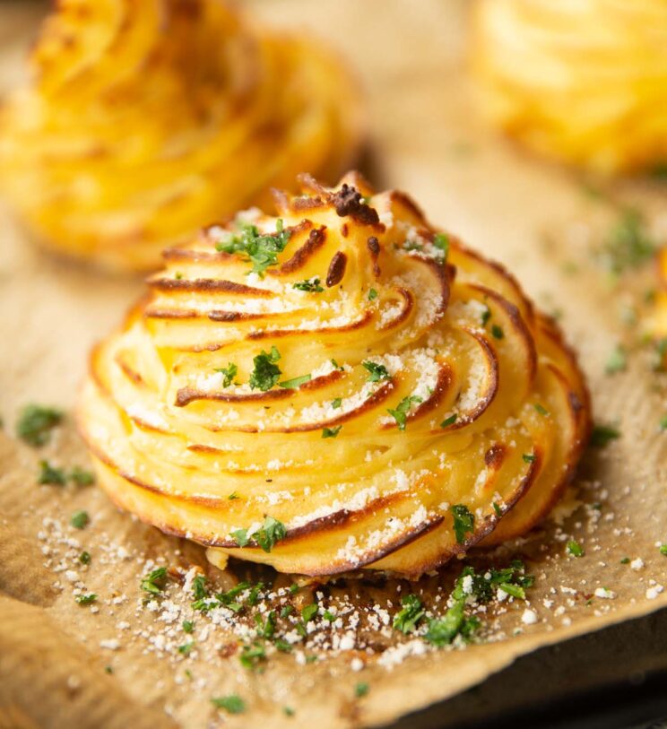 close up shot of duchess potato on baking sheet with parmesan and parsley