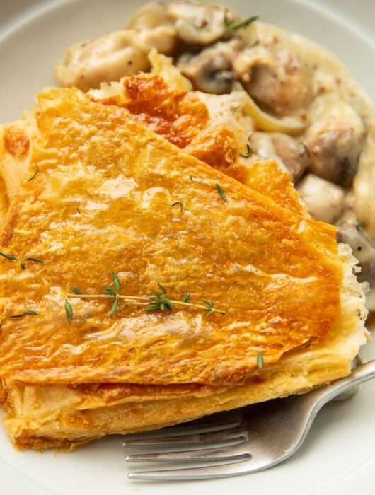 close up shot of chicken and mushroom pie garnished with fresh thyme in large white bowl