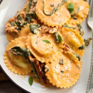close up shot of creamy tuscan ravioli on small white plate