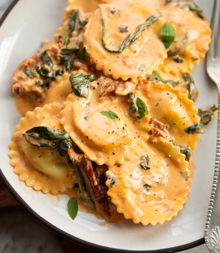close up shot of creamy tuscan ravioli on small white plate