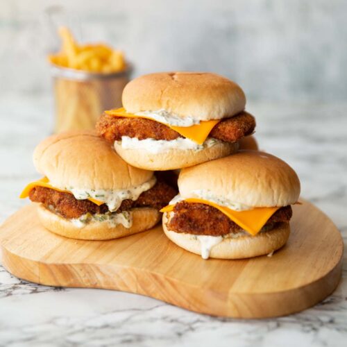 3 homemade filet-o-fish stacked on each other on wooden board with fries in the background