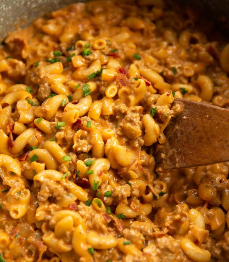 close up shot of hamburger helper in large pot with wooden spoon digging in