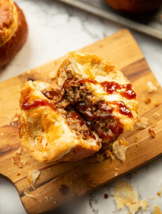 close up shot of beef bread roll pie in half on chopping board with brown sauce