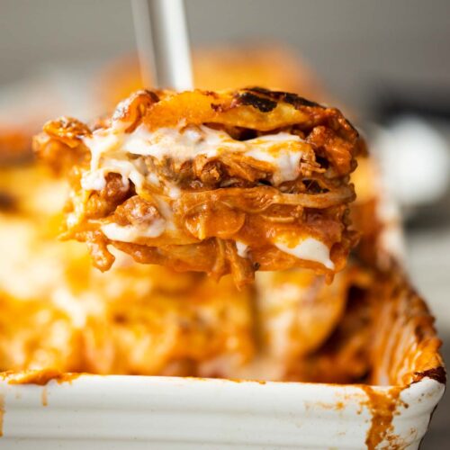 close up shot of metal spatula scooping chicken lasagne out of baking dish