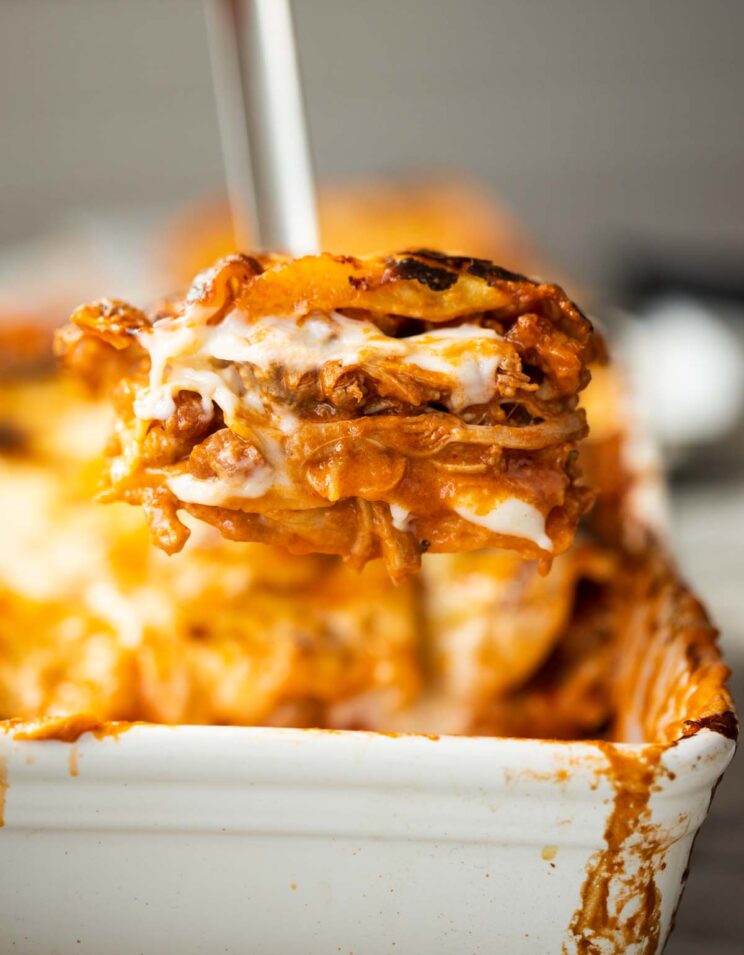 close up shot of metal spatula scooping chicken lasagne out of baking dish