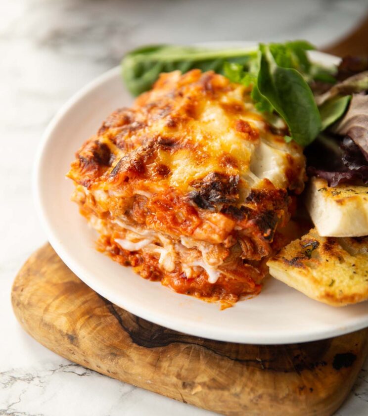 chicken pancetta lasagne served on small white plate with salad and garlic bread