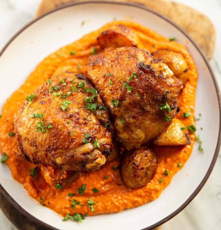 overhead shot of chicken potatoes and romesco sauce on small white plate