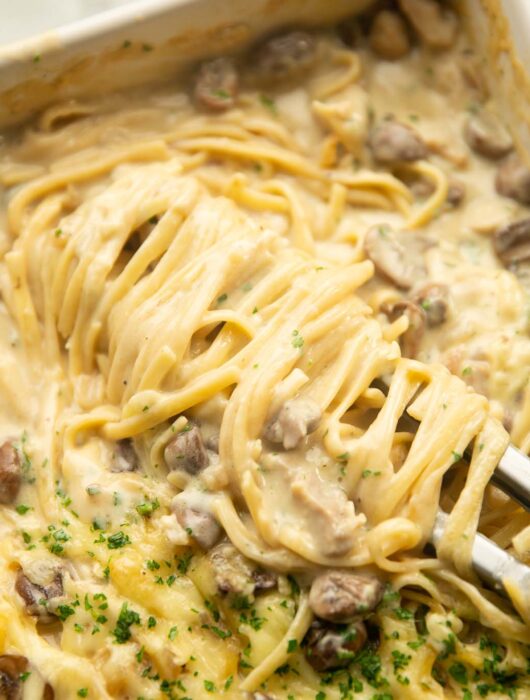 close up shot of pasta tongs twirling chicken tetrazzini in baking dish