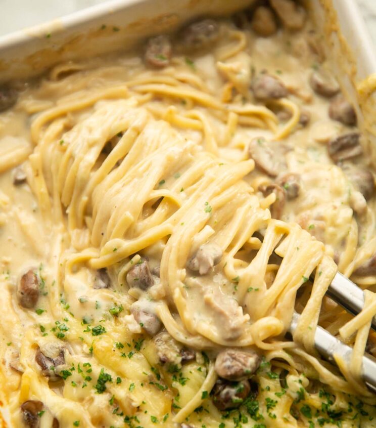 close up shot of pasta tongs twirling chicken tetrazzini in baking dish