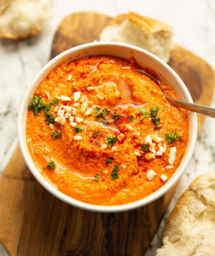 romesco sauce in large white bowl garnished with parsley smoked paprika and almonds