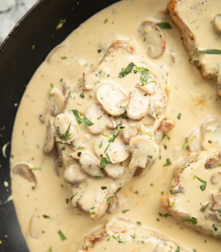 overhead shot of creamy mushroom tarragon pork in pan garnished with more tarragon