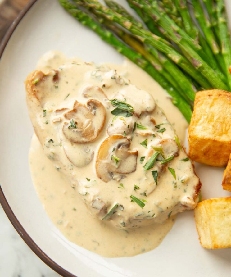 creamy mushroom tarragon pork chop on small white plate with potatoes and asparagus