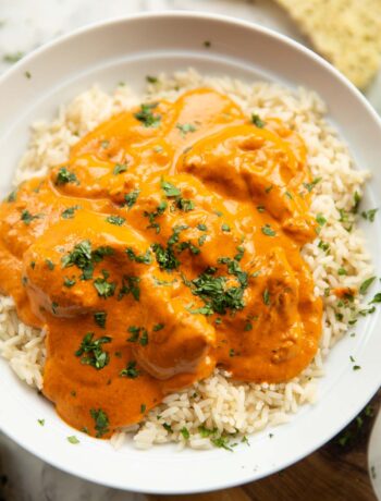 close up shot of homemade butter chicken served on rice in large white bowl