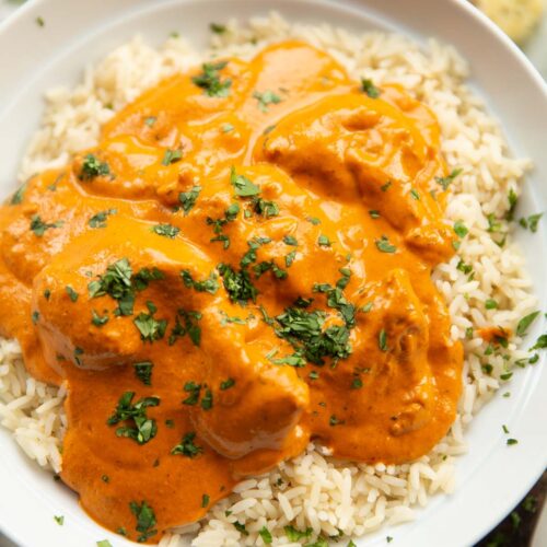 close up shot of homemade butter chicken served on rice in large white bowl
