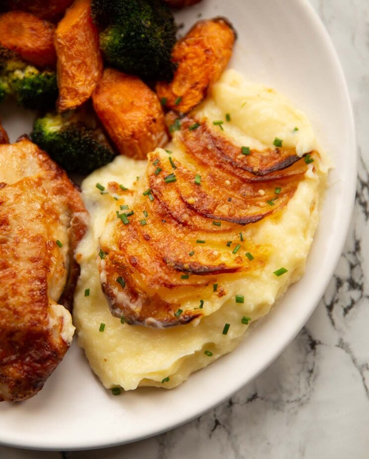 close up shot of mash potato gratin served on small white plate with chicken thighs, carrots and broccoli