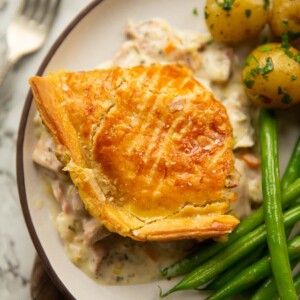 overhead shot of chicken and ham pie served on white plate with potatoes and green beans