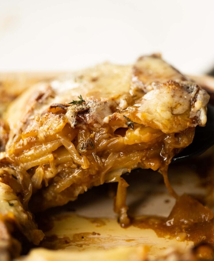 close up shot of spatula lifting french onion boulangere potatoes from baking dish