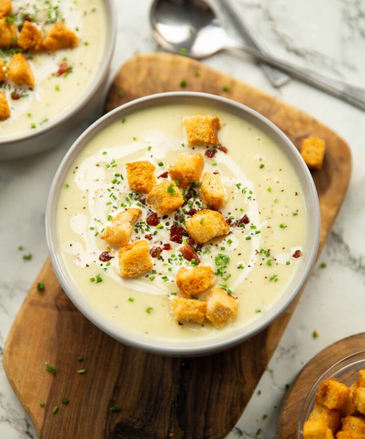 leek and potato soup served in small white bowl on wooden chopping board