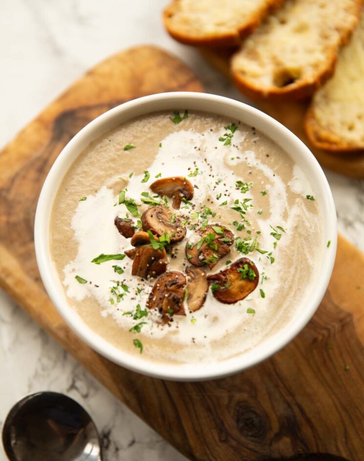 mushroom soup served in small white bowl on wooden chopping board with gruyere crostini