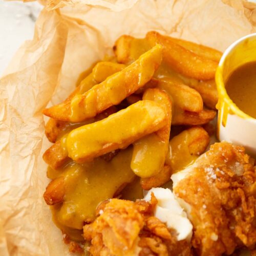 fish and chips covered in curry sauce in scrunched up baking paper