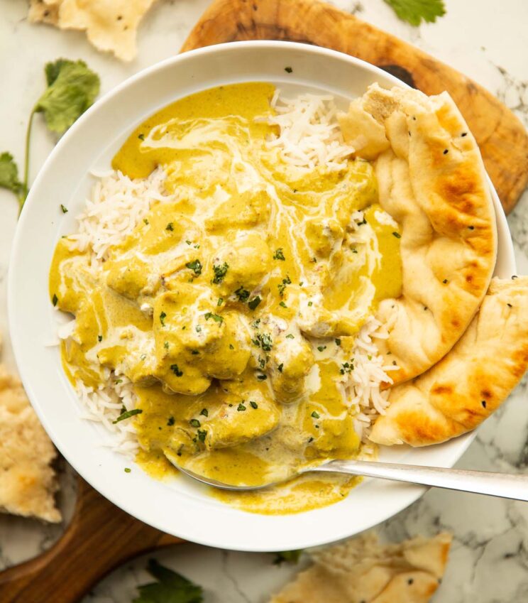 overhead shot of chicken korma in large white bowl with rice and naan 
