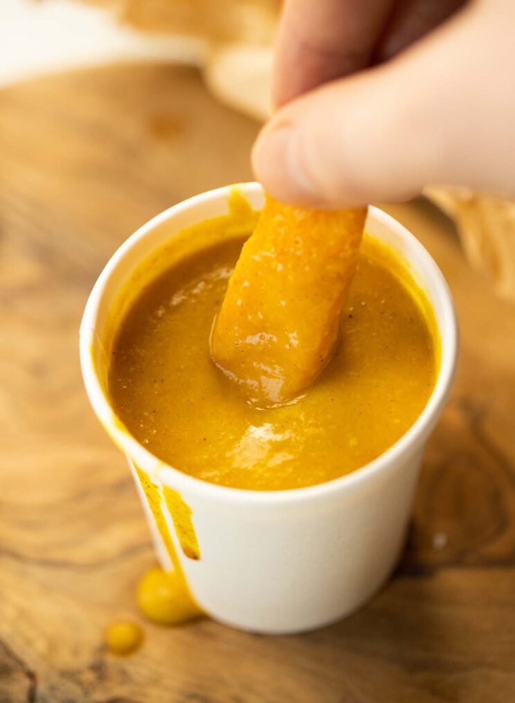 fingers dunking a chip into small pot of chip shop curry sauce