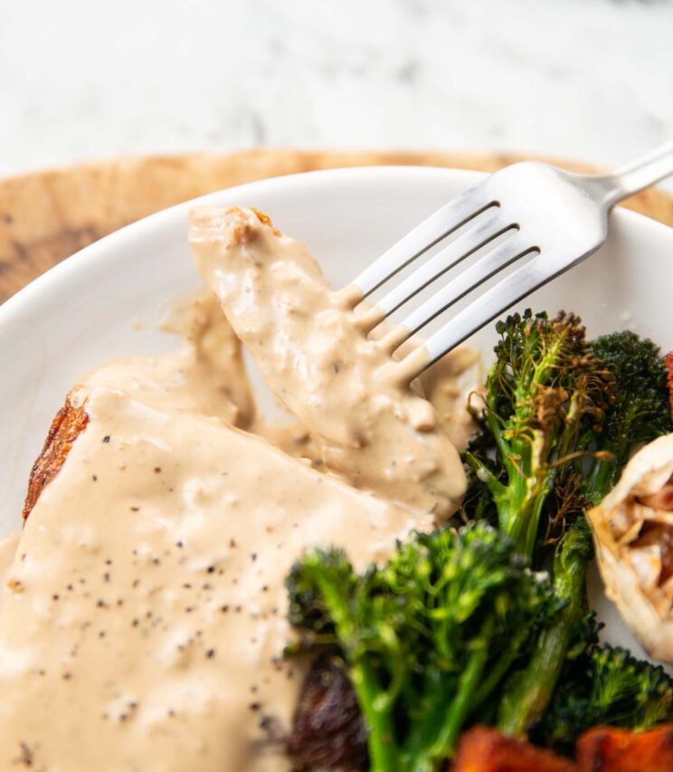 close up shot of silver fork digging into steak covered in sauce