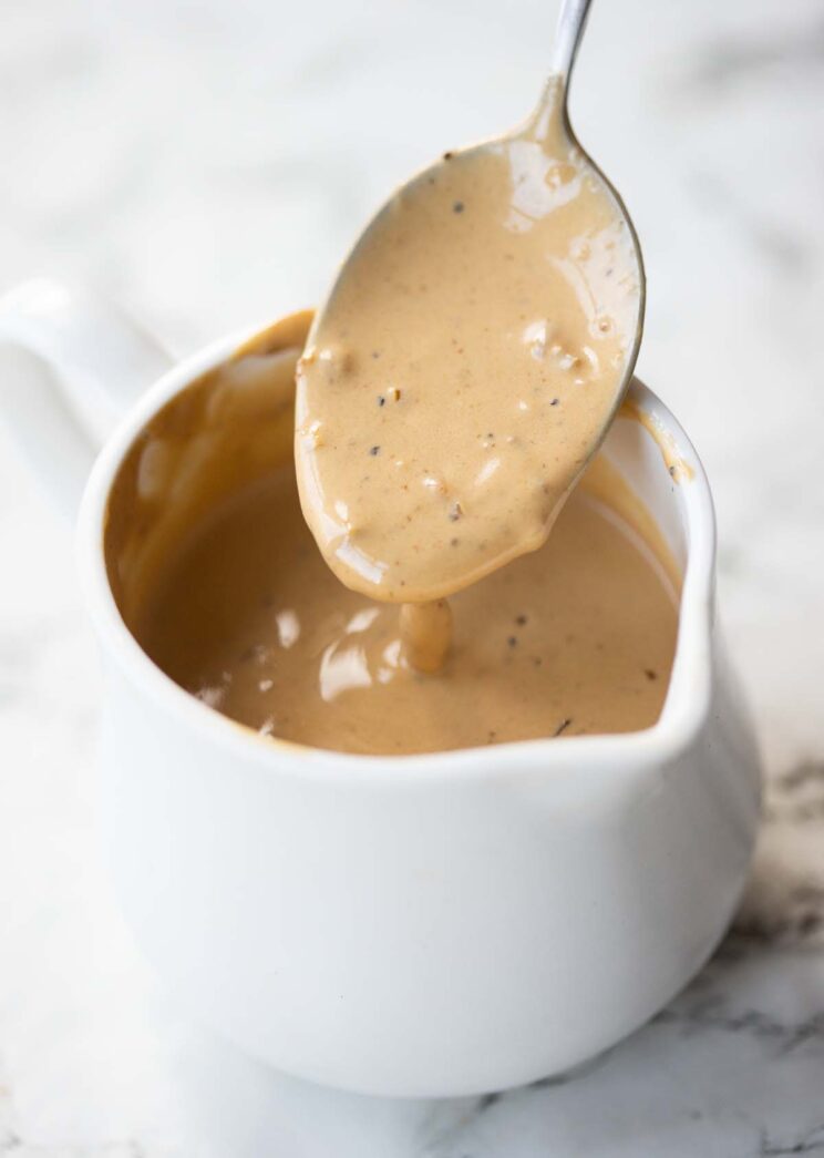 silver spoon dunking into small white jug of creamy garlic steak sauce