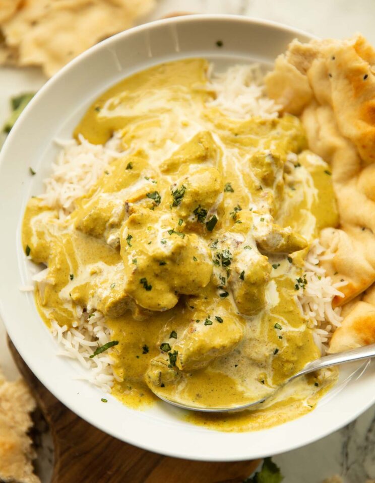 close up shot of chicken korma in large white dish on rice with naan bread
