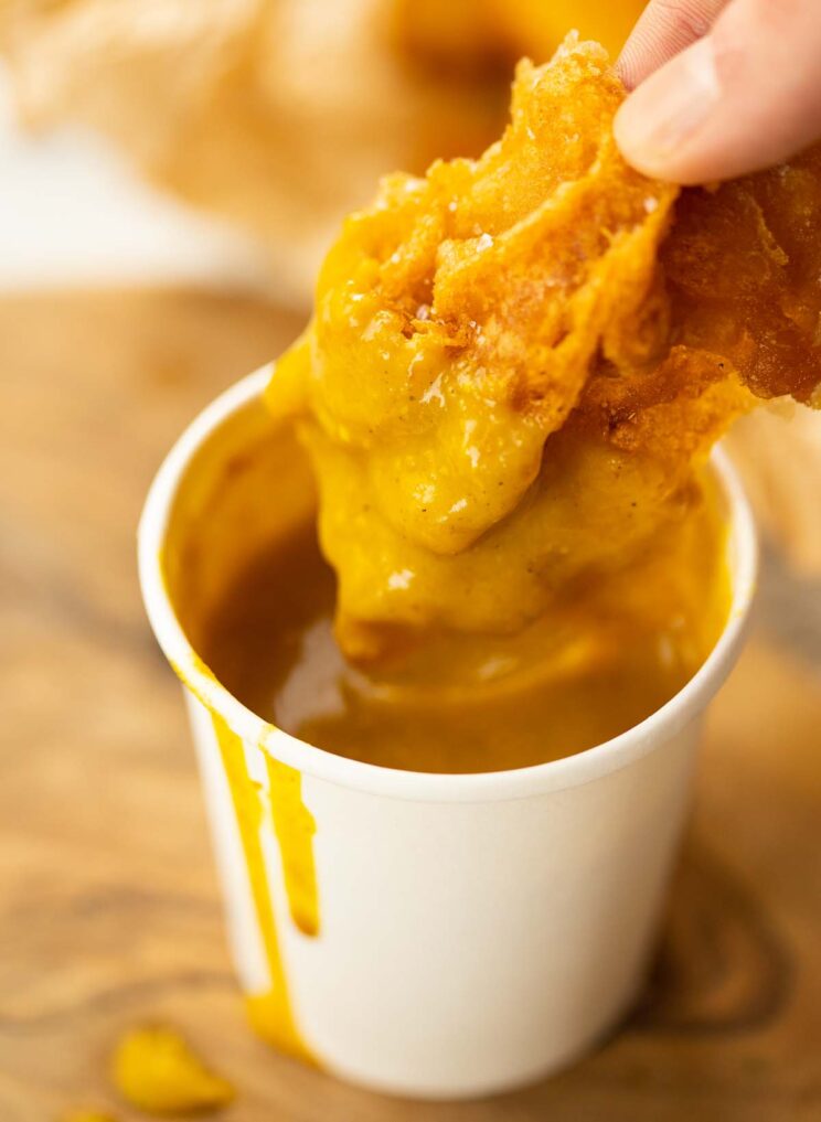 fingers dunking crispy fish into small pot of homemade curry sauce